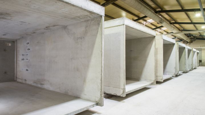 Reihe von Betonelementen in einem Lagerhalleninneren, Rohbauzustand, Deckeninstallationen sichtbar.
