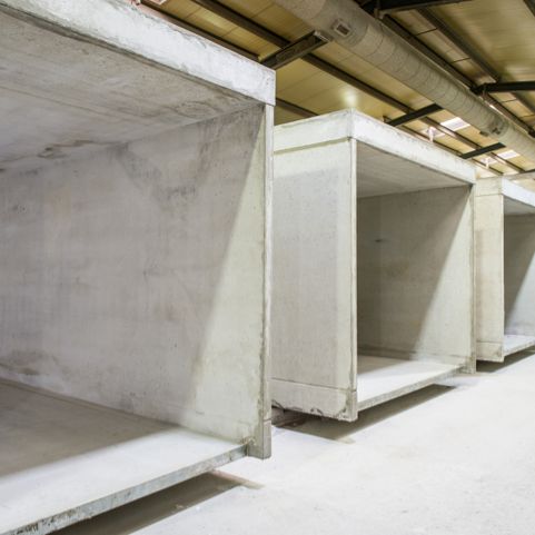 Reihe von Betonelementen in einem Lagerhalleninneren, Rohbauzustand, Deckeninstallationen sichtbar.