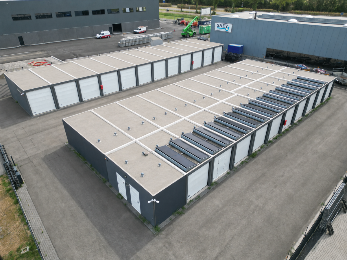 Luftaufnahme einer Lagerhalle mit flachem Dach, Solarpanels und gepflastertem Vorplatz. Im Hintergrund weitere Industriegebäude.