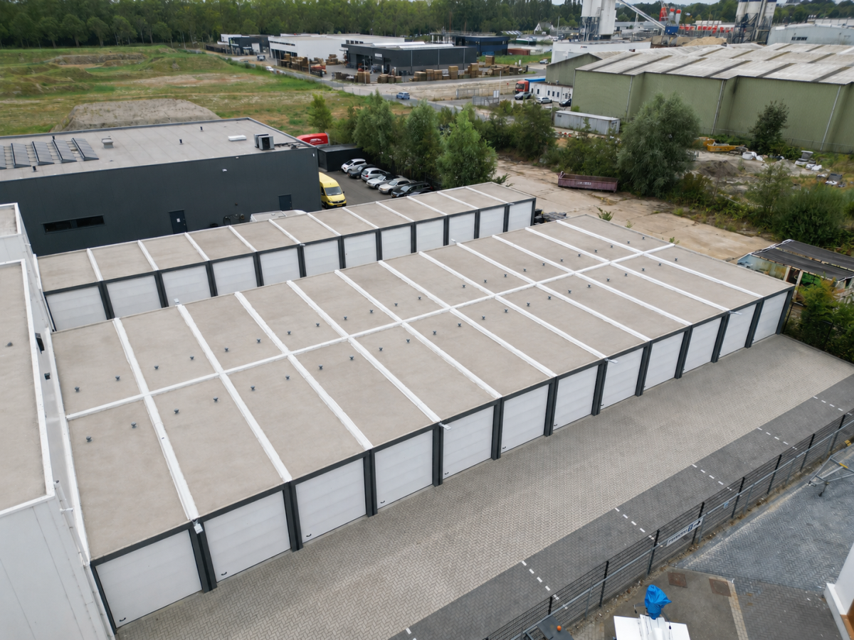 Luftaufnahme eines Gewerbegebiets mit langen, flachen Lagerhallen mit weißen Rolltoren und angrenzenden Gebäuden.