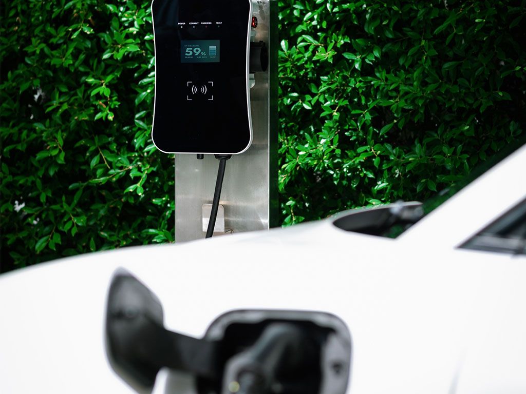 Weiße Elektroauto-Ladefläche an Wand mit Hecken. Display zeigt 59% Ladezustand.