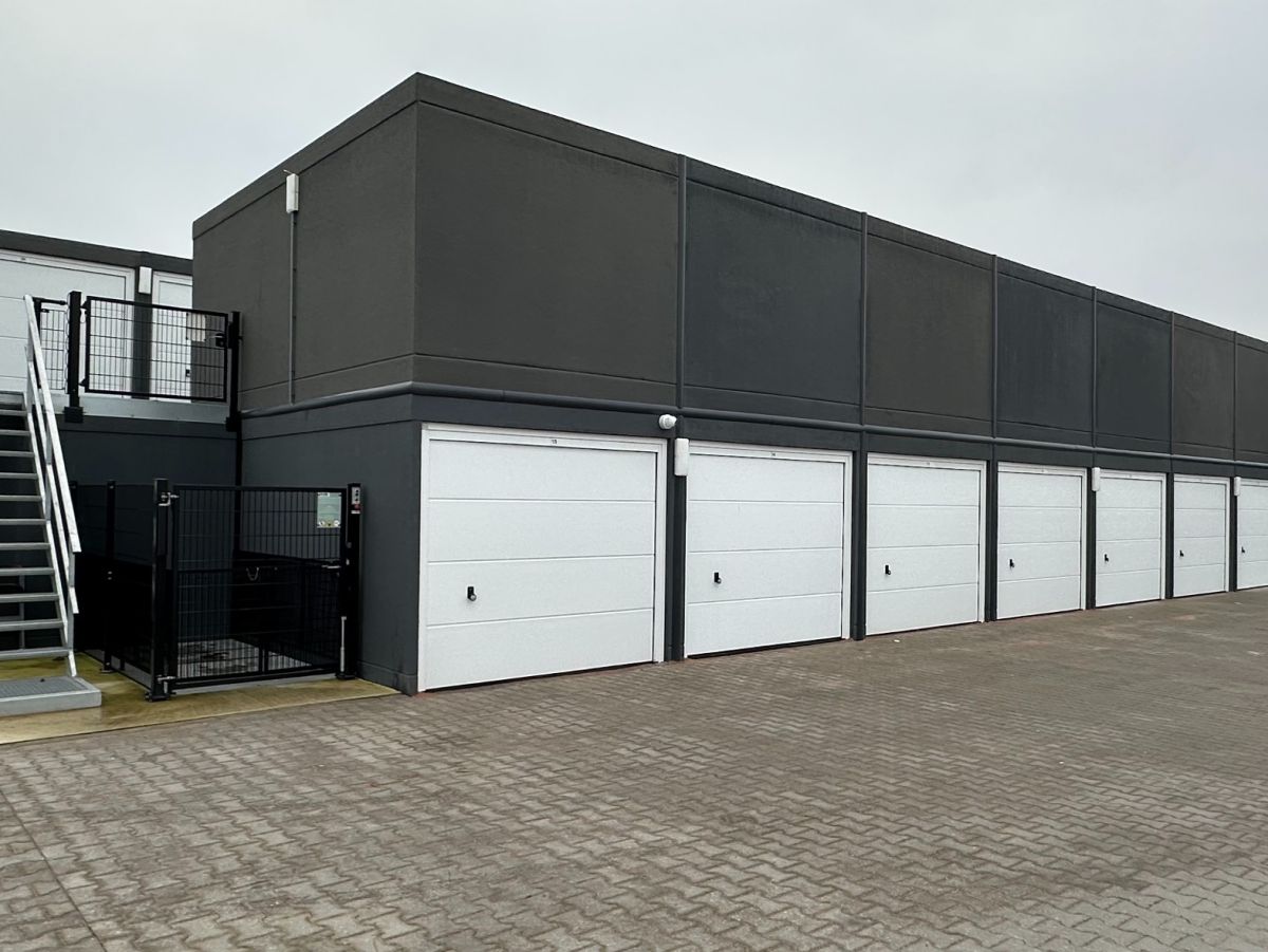 Eingeschossiger Garagenbau mit sechs weißen Garagentoren und Treppe zum Dach.