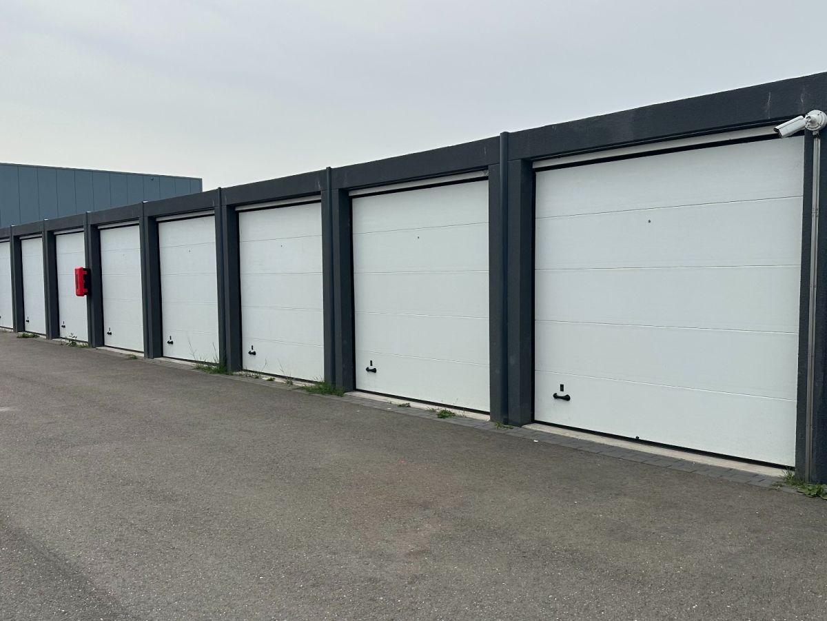 Reihe von weißen Garagentoren mit schwarzem Rahmen, davor Asphaltfläche.