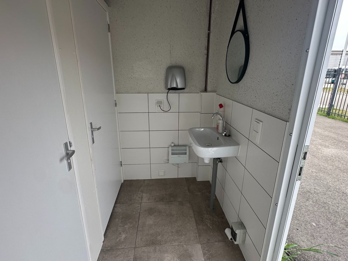 Einfacher Waschraum mit Waschbecken, Spiegel und Tür. Fliesenwände und -boden.