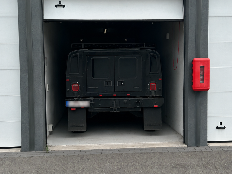 Dunkler Geländewagen fährt in Garage. Links und rechts daneben weitere Garagen.