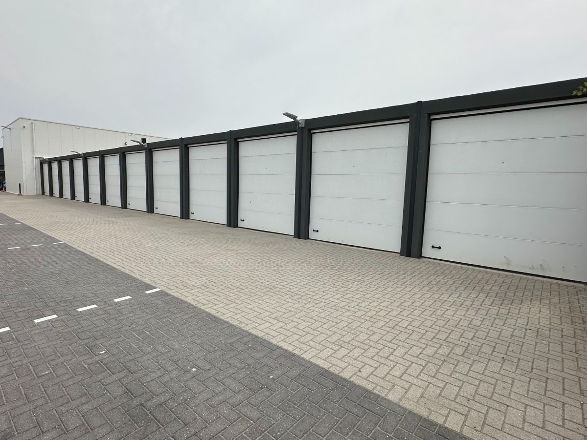 Reihe von weißen Garagentoren mit grauen Rahmen an einer gepflasterten Straße.