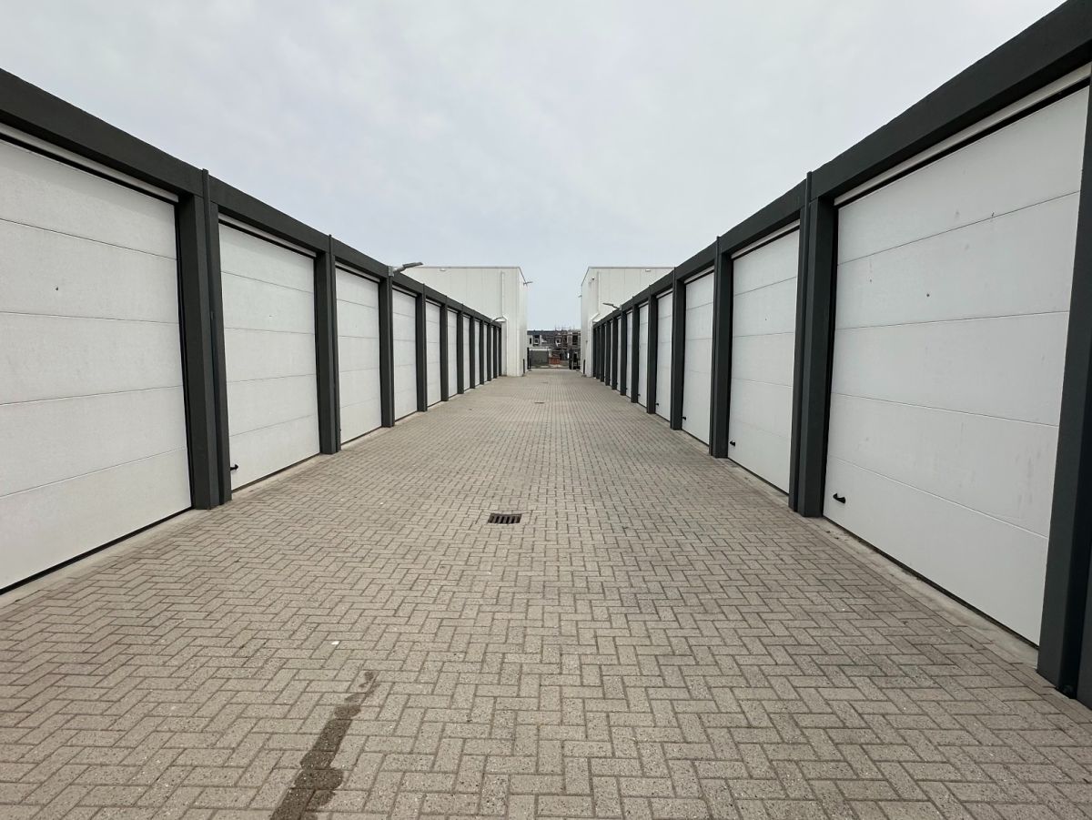 Reihe von weißen Garagentoren mit grauen Rahmen, gepflasterter Weg dazwischen, trüber Himmel.