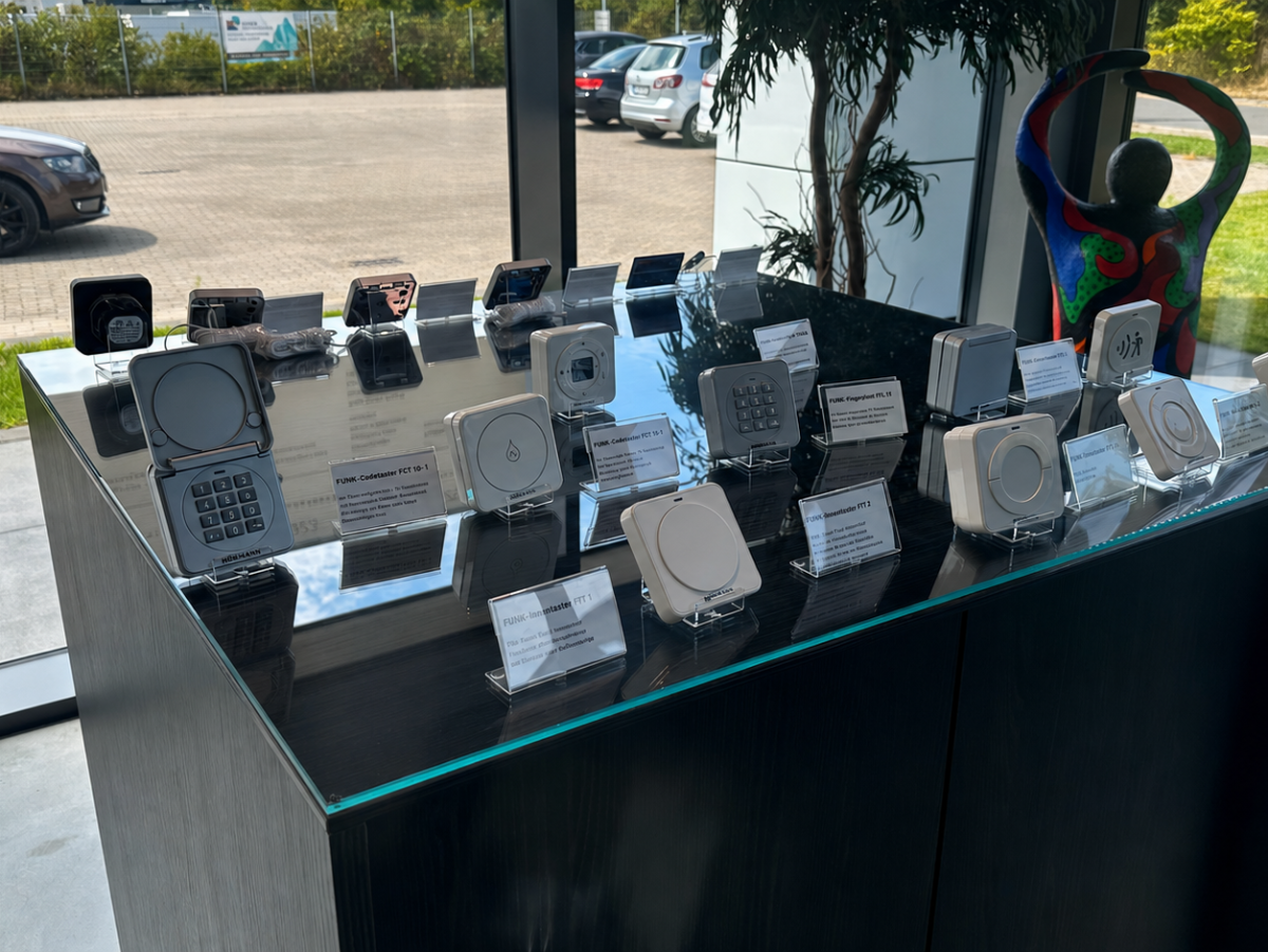 Präsentation von Türsprechanlagen in einer Glasvitrine. Im Hintergrund Autos und Grünflächen.