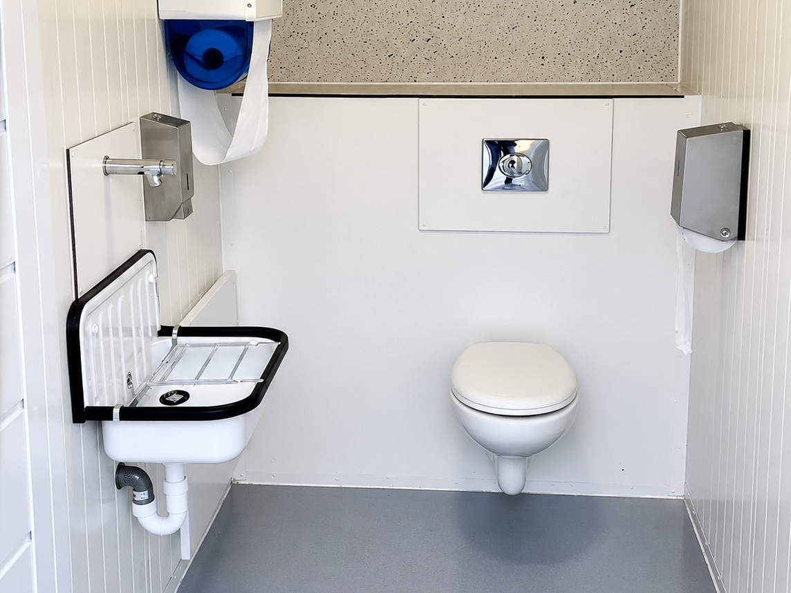 Barrierefreies WC mit wandhängendem WC, klappbarem Waschtisch und Handtuchspender.