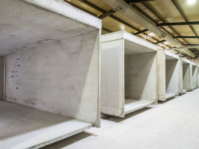 Reihe von Betonelementen in einem Lagerhalleninneren, Rohbauzustand, Deckeninstallationen sichtbar.