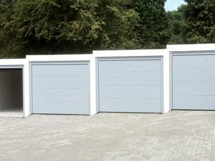 Reihenhaus mit vier Garagen. Eine Garage ist geöffnet, die anderen drei sind geschlossen. Vor den Garagen Pflastersteine.