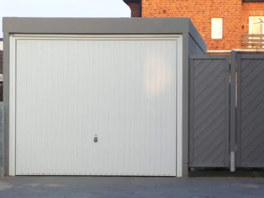 Ein Garagengebäude mit weißen Rolltoren und grauen Seitentoren an einer gepflasterten Auffahrt. Im Hintergrund ein Backsteinhaus.