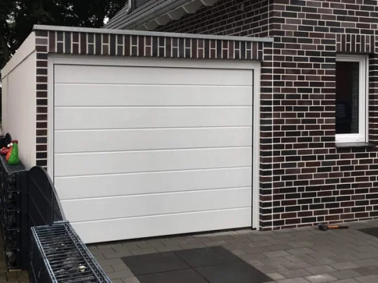 Modernes Haus mit weißer Garage und dunklem Mauerwerk. Fenster rechts der Garage.