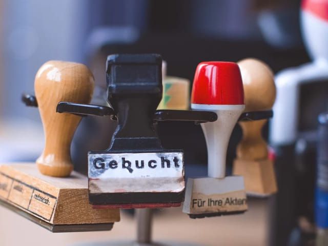Mehrere Stempel liegen übereinander. Vorderster Stempel zeigt den Text 'Gebucht'.