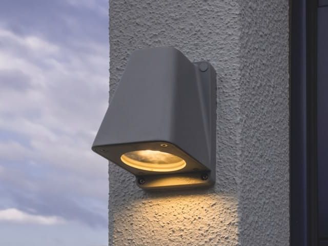 Wandleuchte an einer verputzten Fassade. Das Licht leuchtet warm nach unten.