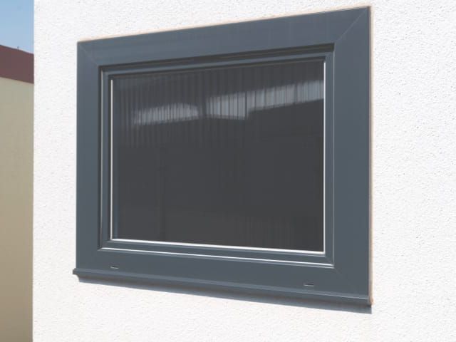 Quadratisches Fenster mit grauem Rahmen an einer hellen Fassade.