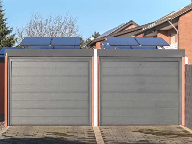Doppelgarage mit grauen Rolltoren und Solaranlage auf dem Dach. Vorgelagerte Pflasterung.
