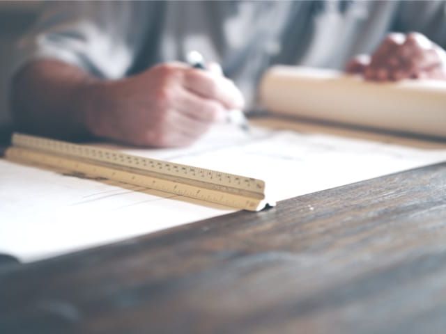 Architekt arbeitet an Bauplänen auf einem Holztisch. Lineal liegt auf den Plänen.