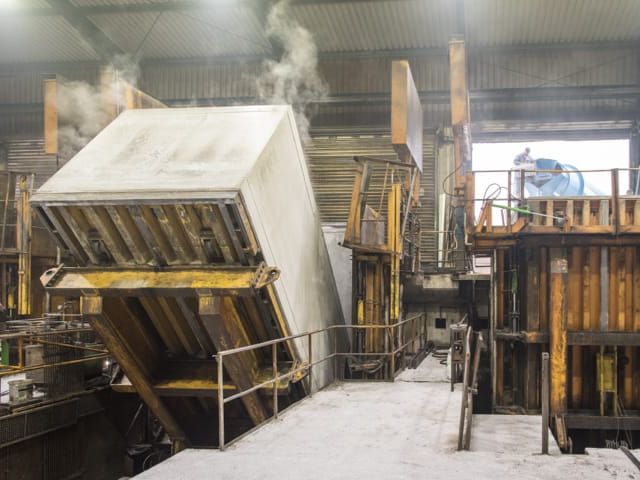 Industriehalle mit schräg stehender, großer Betonform. Arbeiter sind erkennbar, Dampf steigt auf.