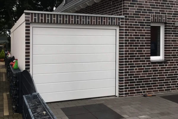 Modernes Haus mit weißer Garage und dunklem Mauerwerk. Fenster rechts der Garage.